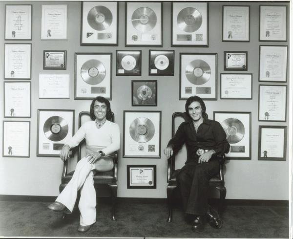 Donald and Richard Addrisi seated in front of a wall filled with framed gold records and award certificates